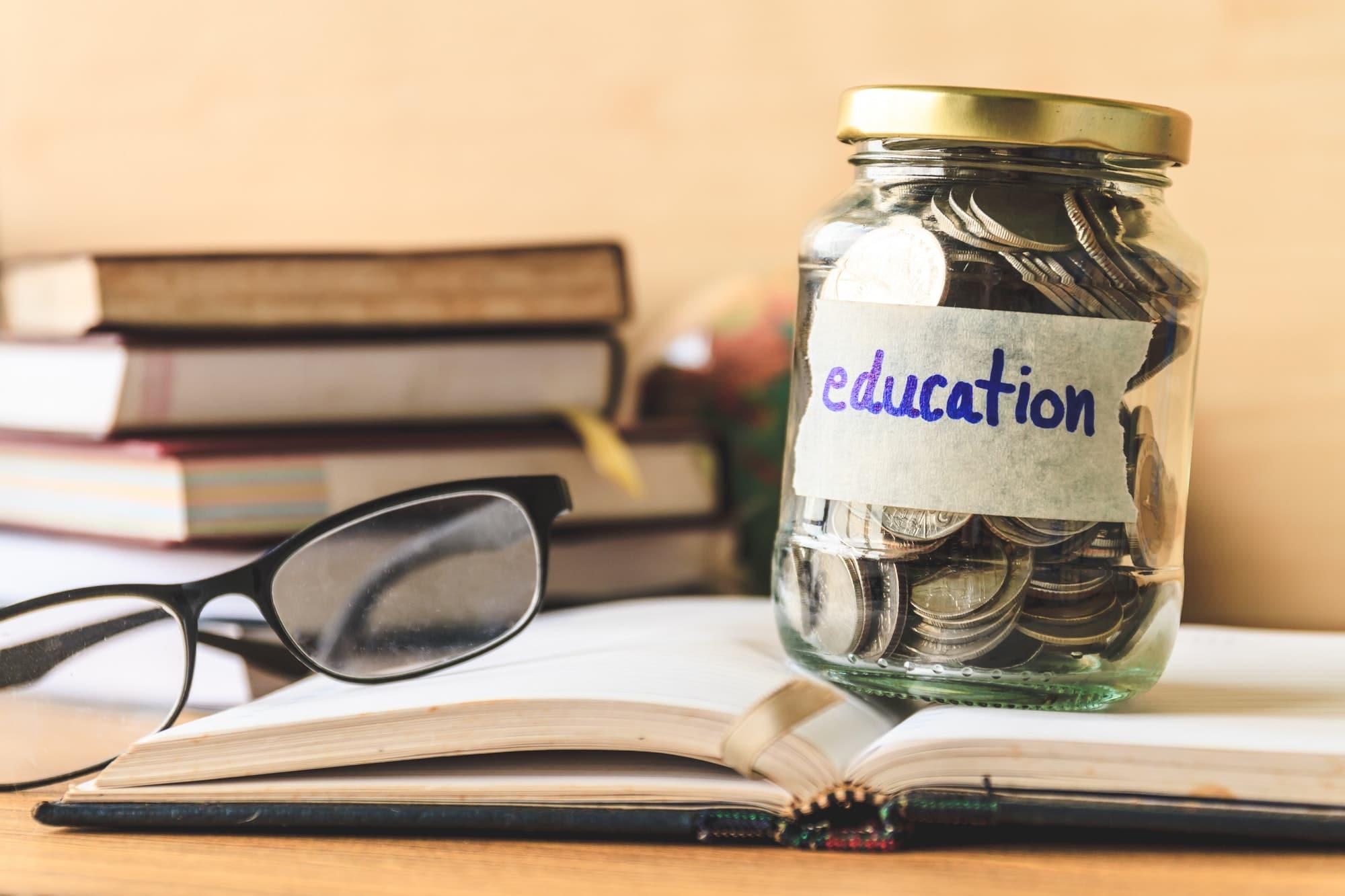 Coins in glass jar with education label, books,glasses and globe on wooden table. Financial concept.