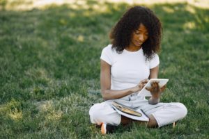 Female african student sitting on a grass and using a tablet