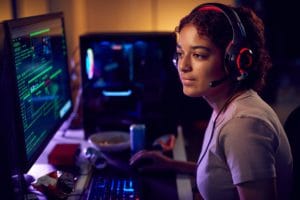 Female Teenage Hacker Sitting In Front Of Computer Screens Bypassing Cyber Security